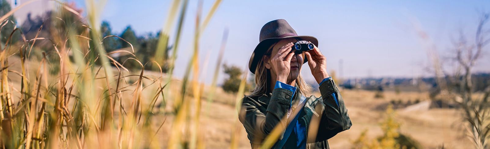 Woman with safari hat standing in Inspiration field with binoculars.